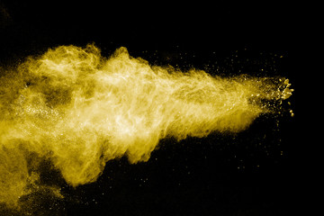 Abstract yellow powder explosion on black background.Freeze motion of yellow dust particles splash.