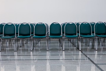 Eye level and front view of several row of dark green chairs on polished floor tiles in waiting...