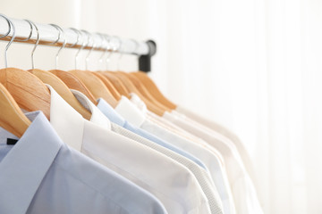Hangers with shirts against light background, copy space