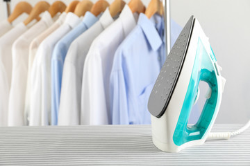 Iron on ironing board against light background, space for text