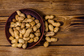 Ceramic plate with heap of unpeeled peanuts on wooden table. Top view