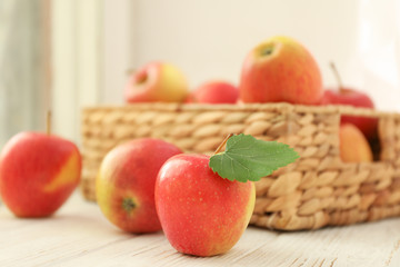 Red apples and wicker basket on wooden background, space for text 