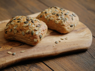 Two sourdough rolls with pumpkin seed on a wooden board and table, Warm brown tones. Bakery product. Close up.