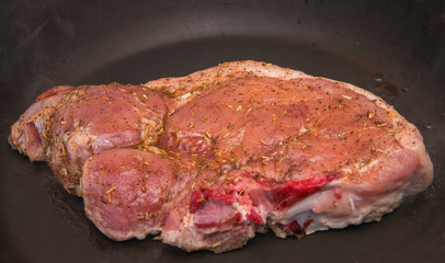 Fresh raw pork steak with spices roasting on the black frying pan in the kitchen