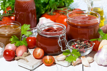 assortment of tomato sauces and ingredients on white wooden background, closeup