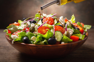olive oil pouring into bowl of fresh salad with vegetables, feta cheese and capers