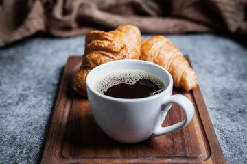 Breakfast with fresh croissants and cup of black coffee on wooden board