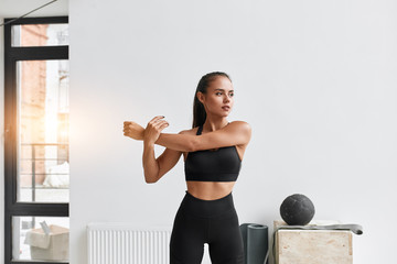 Slim caucasian female in black sportswear warm-up muscles prapering to do exercises, cross fit. White gym background - obrazy, fototapety, plakaty
