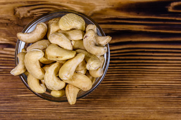 Glass bowl with raw cashew nuts on a wooden table. Top view