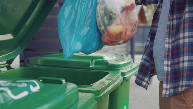 Caucasian Man is Walking Outside His House in Order to Take Out Two Plastic Bags of Trash. One Garbage Bag is Sorted into Biological Food Waste, Other is Thrown into Recyclable Bottles Garbage Bin.