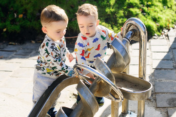 Two-year-old twin brothers explore the metal construction of the Archimedes screw. They are focused and serious.
