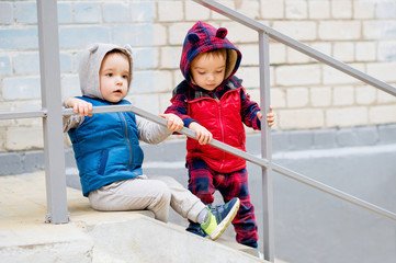 Brightly dressed two-year-old twin brothers playing on the stairs. They smile cheerfully.