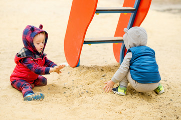 Two-year-old brightly dressed twin boys play on the playground