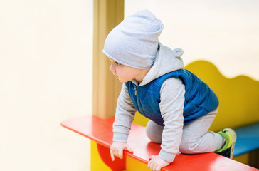 Two-year-old brightly dressed boy is playing on the playground