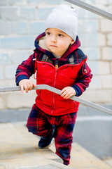 A brightly dressed two-year-old baby is playing on the stairs. He smiles cheerfully.