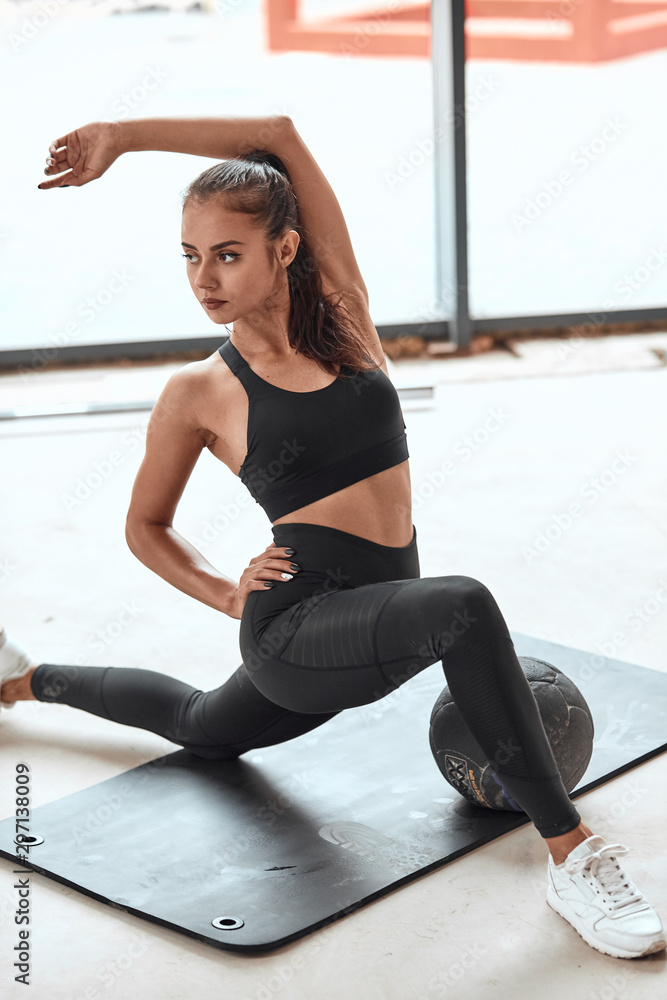 Wall mural Young female training in gym, do fitness exercises. Hands over head. Lunges on mat using balls. window background