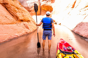 Kayaking hiking trail in Lake Powell narrow and shallow antelope canyon with man holding paddle oar standing in dirty muddy water and rock formations © Kristina Blokhin