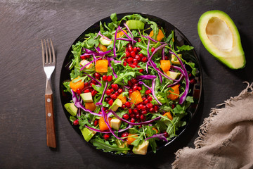 plate of fresh salad with rucola, pomegranate seeds, avocado, pumpkin and purple cabbage, top view
