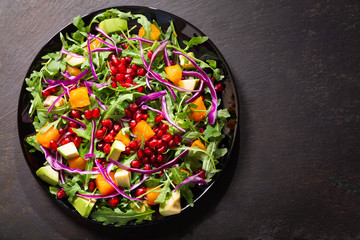 plate of fresh salad with rucola, pomegranate seeds, avocado, pumpkin and purple cabbage, top view