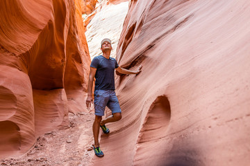 Man hiker looking up touching wall of red wave shape formations at Antelope slot canyon in Arizona on footpath trail from Lake Powell © Kristina Blokhin