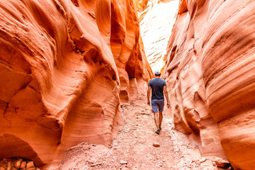 Man hiker walking by red wave shape formations at Antelope slot canyon in Arizona on footpath trail...