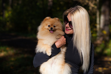 Happy young fashion woman with dwarf spitz in autumn forest