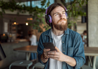 Dreamingly concentrated bearded young man looking aside while listening to the music