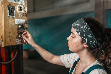 The concept of small business, feminism and women's equality. A young tired woman presses a button on the factory working mechanism