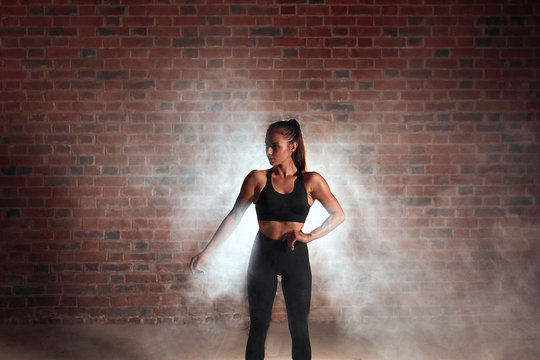 Slim fitness woman in sportswear standing, looking away. Steam background, Posing
