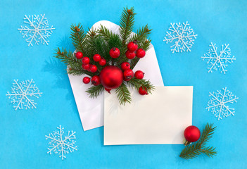Fototapeta na wymiar Christmas decoration. Balls, christmas tree, red berries in postal envelope, blank sheet with space for text on a blue paper background with snowflakes. Top view, flat lay