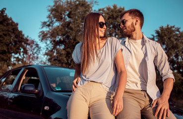 Young man and woman talking while sitting on a car hood on a countryside road