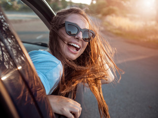 Young pretty brown-haired girl enjoys feeling the wind while leaning out of the car window