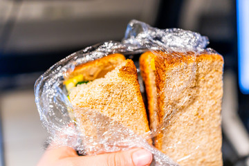 Closeup of hand holding plastic wrapped whole wheat grain bread in airplane flight with crust and vegetable filling as vegan meal