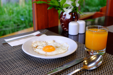 Sunny side up fried egg served on white dish with orange juice for breakfast