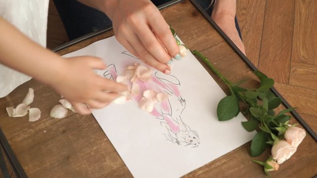 Close up of female and children's hands make natural application in picture, laying out pink flower rose petals. Сoncept of children's creativity, development and decor