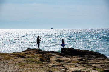 Fototapeta na wymiar A girl and a guy walk on a rock by the sea.