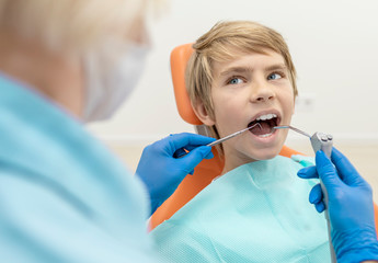 Boy with water spray syringe and dentist probe in his mouth looking at the dentist