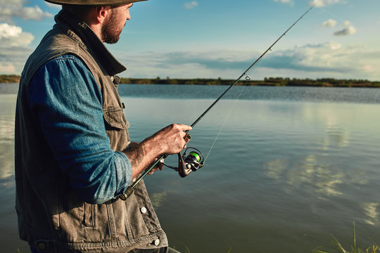 Caucasian adult bearded men stand near lake and hold fishing rod. he looks into distance and at float. Fishing is meditation.