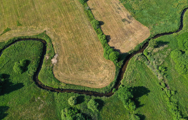 Aerial drone top down view on european green meadows, wheat fields and forest divided by snake like river.