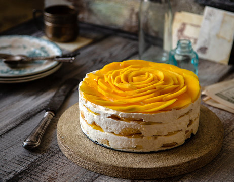 whole round tiramisu cake with white whipped cream and slices of ripe juicy mango on top