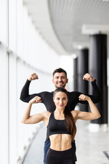 Fototapeta na wymiar Athletic man and woman after fitness exercise show biceps standing at gym