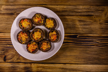 Baked champignons stuffed with minced meat and cheese in plate on a wooden table. Top view