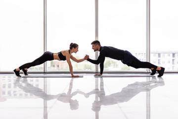 Young sporty couple working out together in a gym doing plank exercises while holding each other for one hand.