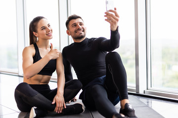 Fototapeta na wymiar Young couple making selfie at gym. Athlete man and woman taking photo on smartphone having break after training,