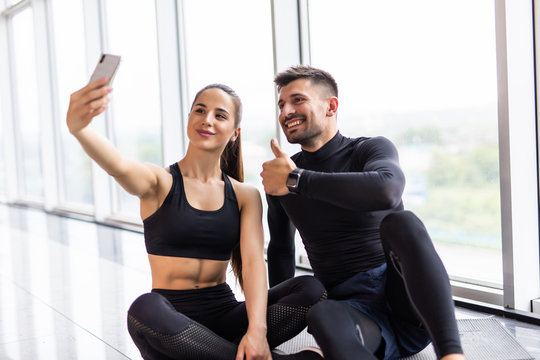Young couple making selfie at gym. Athlete man and woman taking photo on smartphone having break after training,