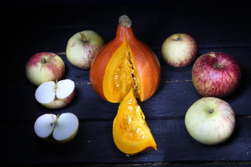 Orange pumpkin with cut part, yellow  and red apples on black background