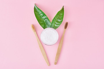 Wooden bamboo toothbrushes with baking soda powder in glass jar and green leaves on a pink background.  Teeth health and keep mouth concept