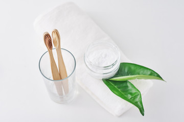 Two wooden bamboo eco friendly toothbrushes in a glass, baking soda and towel on white background.  Dental care and zero waste concept