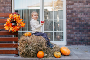 Adorable smiling Caucasian baby toddler in white knittes jacket sitting on the haystack with...