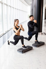 Muscular fitness couple doing jumping squats in crossfit gym